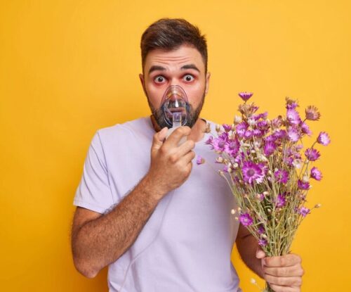 Mężczyzna w jednej ręce trzyma bukiet kwiatów, a w drugiej inhalator