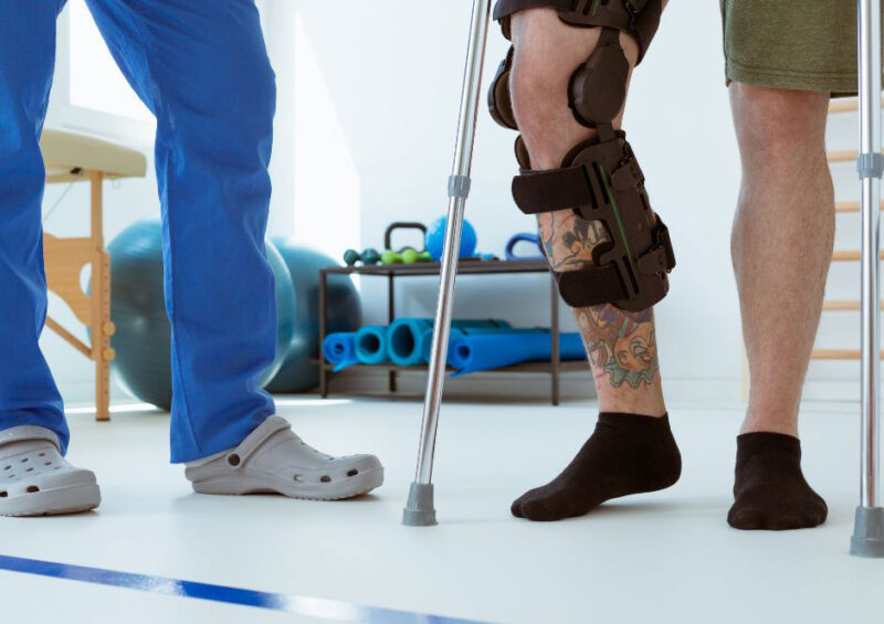 Fizjoterapeuta wspiera w chodzeniu pacjenta w ortezie