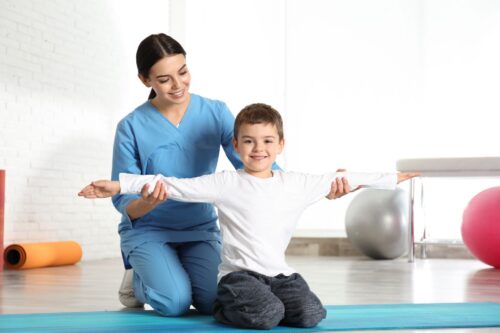 Rehabilitantka przeprowadza rehabilitacje uśmiechniętego chłopca