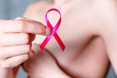 Kobieta trzyma różową wstążkę, symbol walki z rakiem piersi, na tle zakrytej dłonią piersi