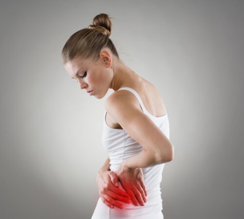 Kobieta w białym topie trzyma bolesne biodro, okolica biodra podświetlona na czerwono